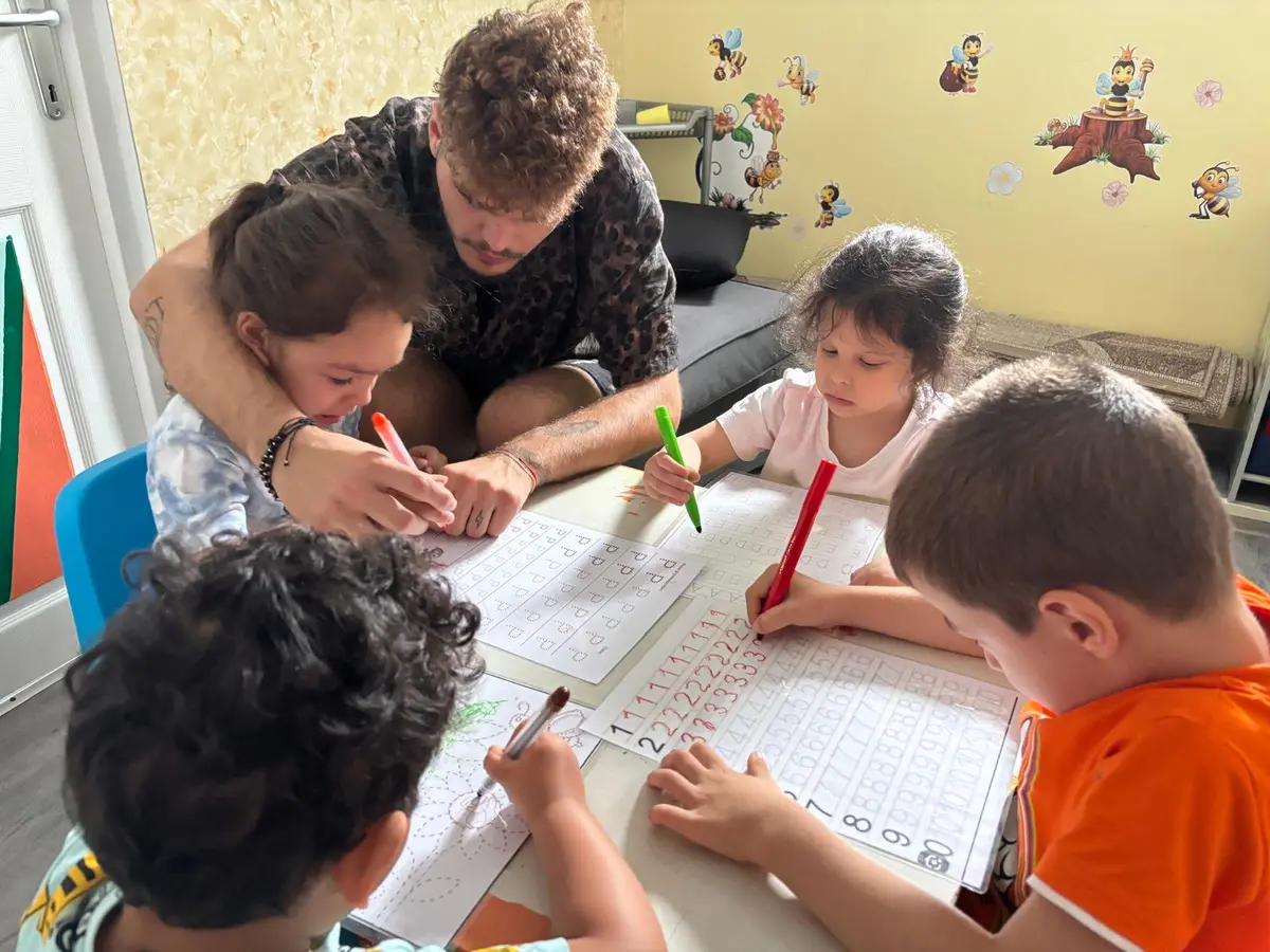 Un voluntar tânăr ajută mai mulți copii la scris